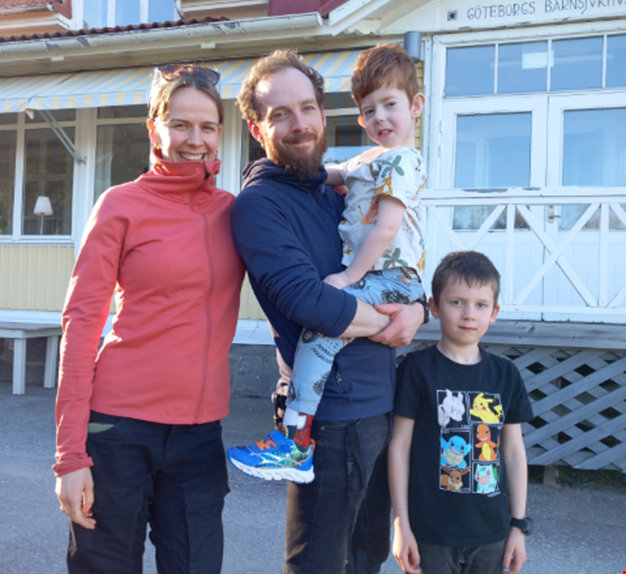 Två föräldrar och två barn framför Gula huset på Ågrenska.