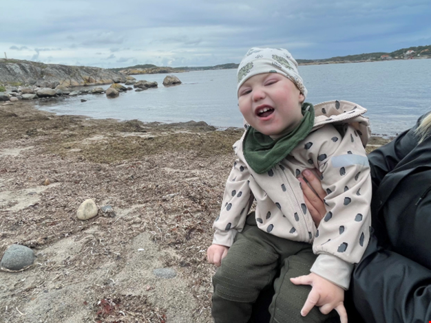 Ett barn sitter i knät på en vuxen vid stranden.