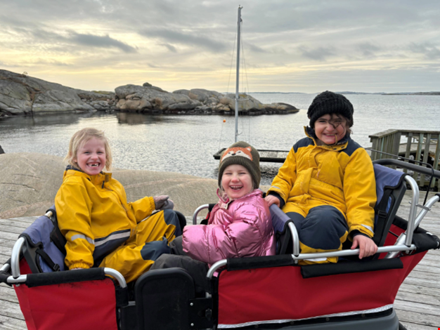 Tre barn som åker i kompisbussen vid havet. 