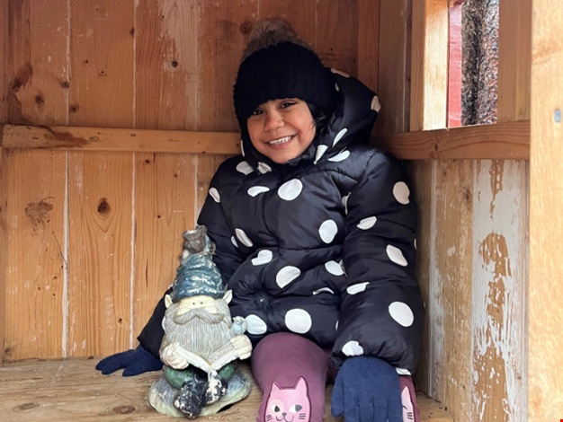 Flicka som sitter på träbänk med trädgårdstomte. 