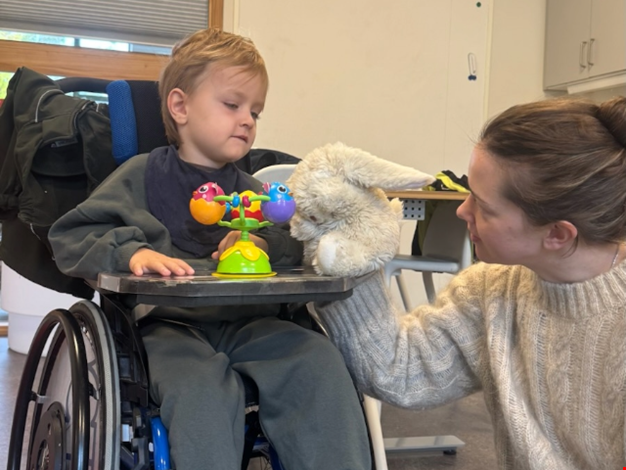 Pojke som sitter i rullstol och hälsar på ett gosedjur i form av en kanin.