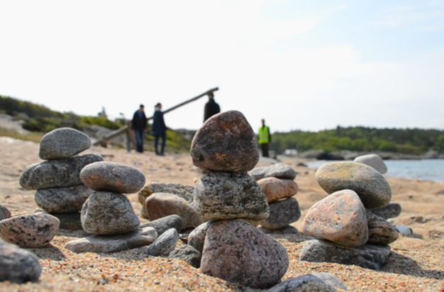 Bild på stenar organiserade i högar på stranden. Människor skymtas i bakgrunden.