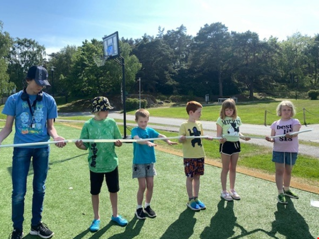 Fem barn och en vuxen leker samarbetslekar på fotbollsplanen. 