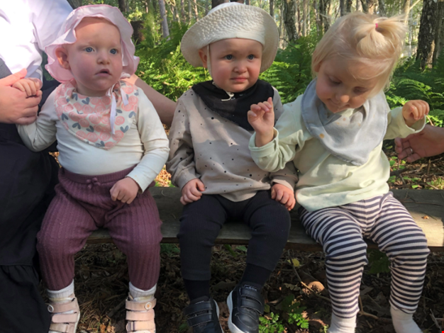 Tre barn sitter på en stock i skolgen.