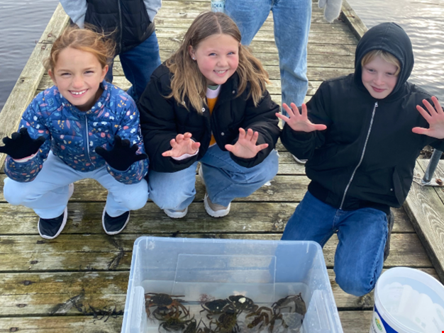 Tre barn visar upp sin krabbfångst. 