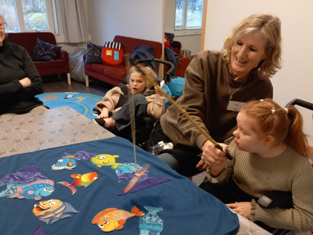 En vxuen och två barn leker med ett fiskspel.