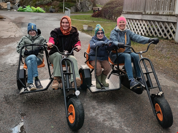 Två barn och två vuxna åker trampbil.