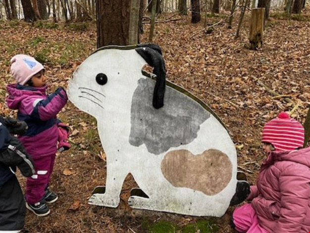 Två barn matar en träkanin med kottar.