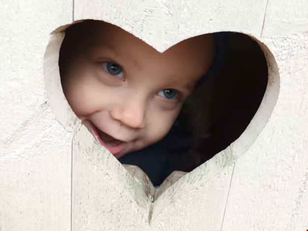 Ett barn kikar ut ifrån ett hjärtformat hål.