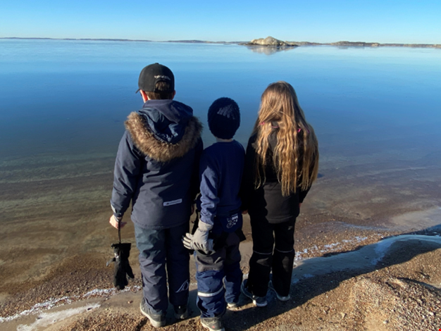 Tre barn som står på en strand och tittar ut över havet.