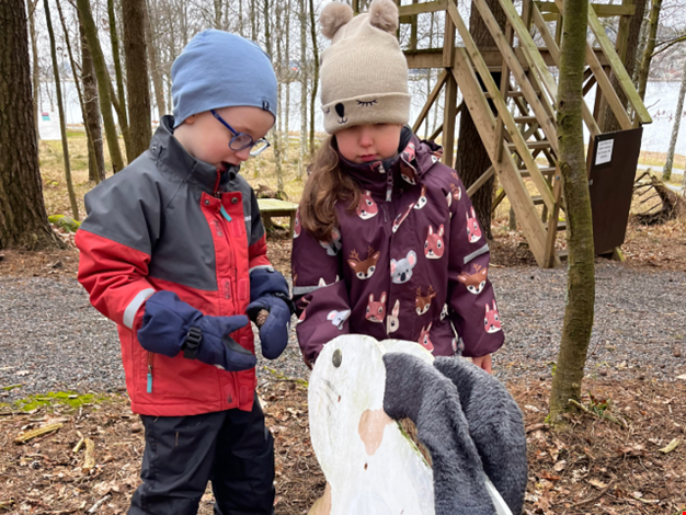 Två barn matar en träkanin med kottar.