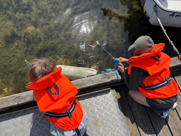 Två barn fiskar krabba i flytväst.