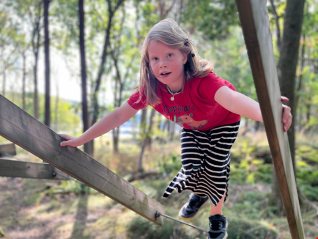 Flicka klättrar på en träställning i skogen.