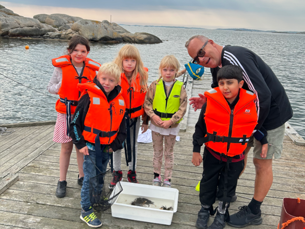 Fem barn och en vuxen står på brygga och har fiskat krabbor.