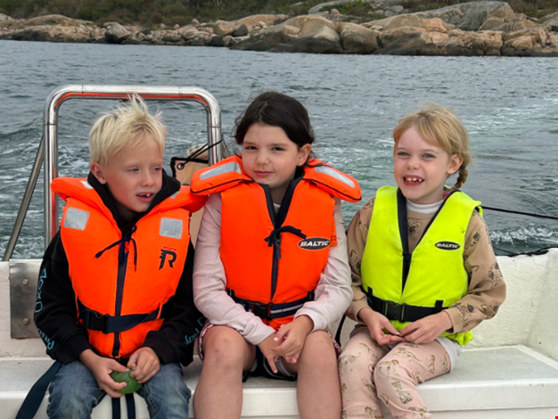 Tre barn i flytväst åker motorbåt på havet. 