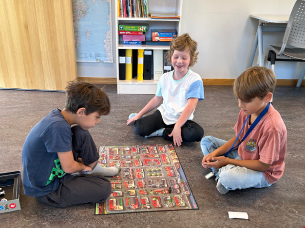 Tre barn sitter på golvet och spelar ett brädspel. 
