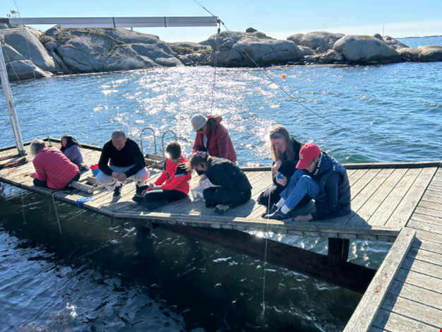 Barn och vuxna sitter vid bryggan och fiskar krabbor. 