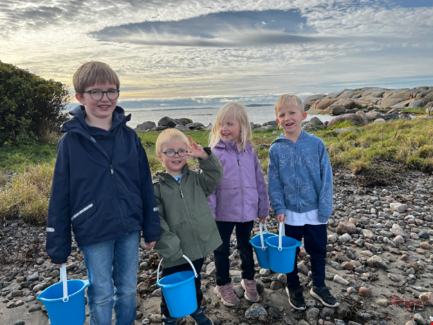 Fyra barn står på stranden och håller i varsin blå hink.