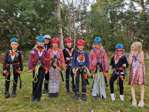 Nio barn står uppradade iklädda sele redo att åka linbana.