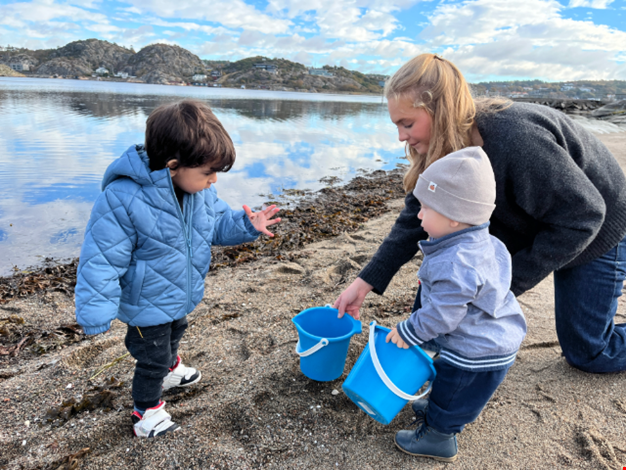 Två barn och en vuxen plockar snäckor på stranden. 