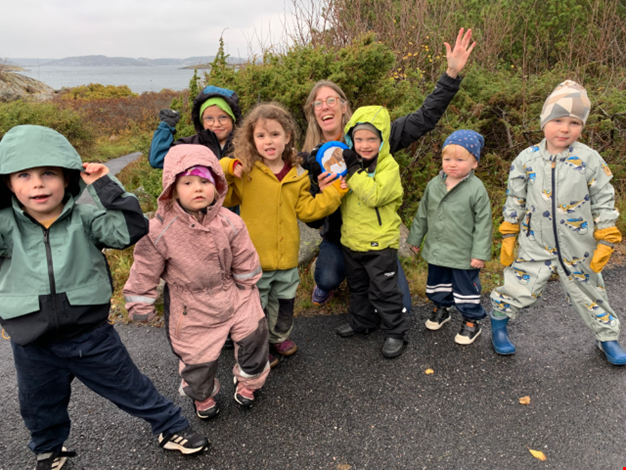 Flera barn och en vuxen på en väg framför havet iklädda regnkläder. 