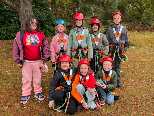 Flera förväntansfulla barn iklädda sele redo för linbana.