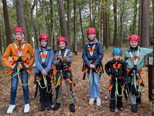 Flera förväntansfulla barn iklädda sele redo för linbana.