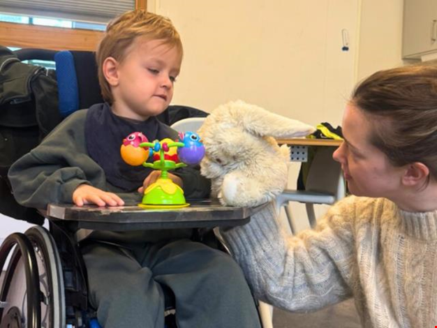 Pojke sitter i rullstol och hälsar på en mjukiskanin. 