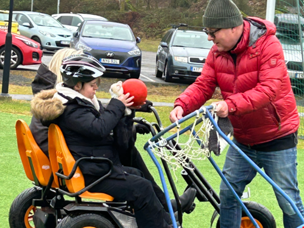 Personal hjälper barn att kasta boll i korg.