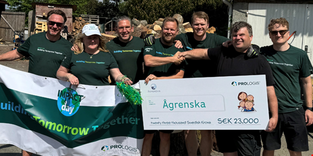 En grupp personer står tillsammans utomhus. Två personer håller upp en stor symbolisk check på 23 000 kronor till Ågrenska, andra håller en banderoll. Alla ler mot kameran.