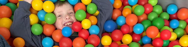 Bild på ett barn som ler och ligger i ett bollhav.