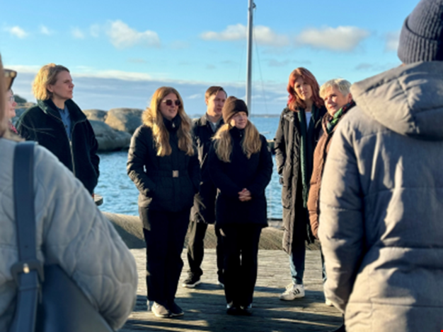 En grupp kursdeltagare som står nere vid Ågrenskas bastu. Havet i bakgrunden.